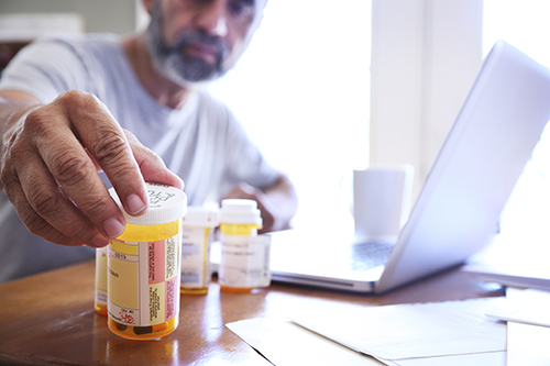 A man sits at a desk and looks at labels on medicines